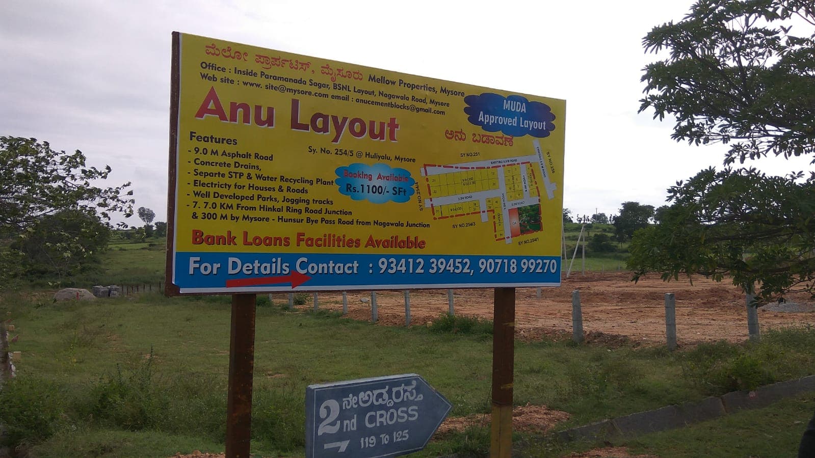Anu Layout site board listing asphalt roads, drains, parks and MUDA approval
